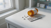 Plain white ivermectin-style oral tablets beside a foil blister strip and an amber prescription vial on a pharmacy counter.