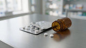 Small plain white ivermectin-style oral tablets in a foil blister strip beside an amber prescription vial on a pharmacy counter.